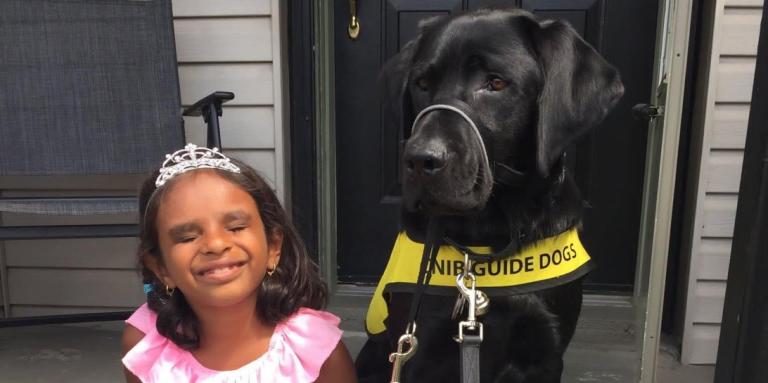 A young girl radiates joy and sits on her front porch stoop alongside her CNIB buddy dog. 