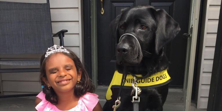 A young girl radiates joy and sits on her front porch stoop alongside her CNIB buddy dog. 