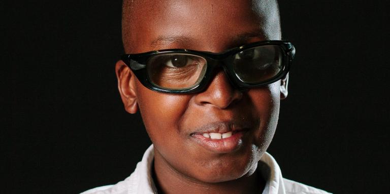 A young boy smiles for a school photo. He is wearing glasses and a polo shirt.