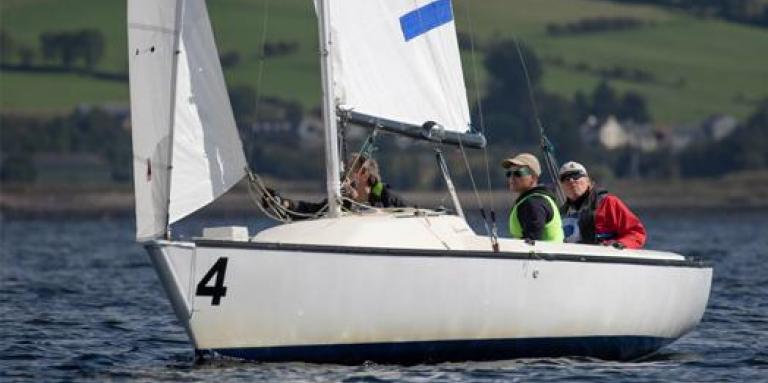 Joshua Cook et deux autres personnes sont assises dans un bateau à voile sur l'eau. Ils sont aux championnats du monde de voile aveugle en Ecosse.