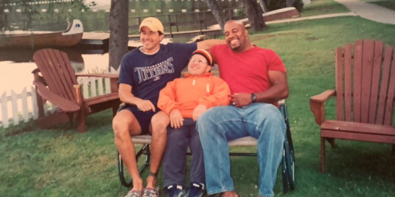 Shawn Dale, Bill Vastis and Derek Thompson sit together on a bench and pose for a group photo on the shoreline of Lake Joe. Their smiles are wide and radiate joy! 