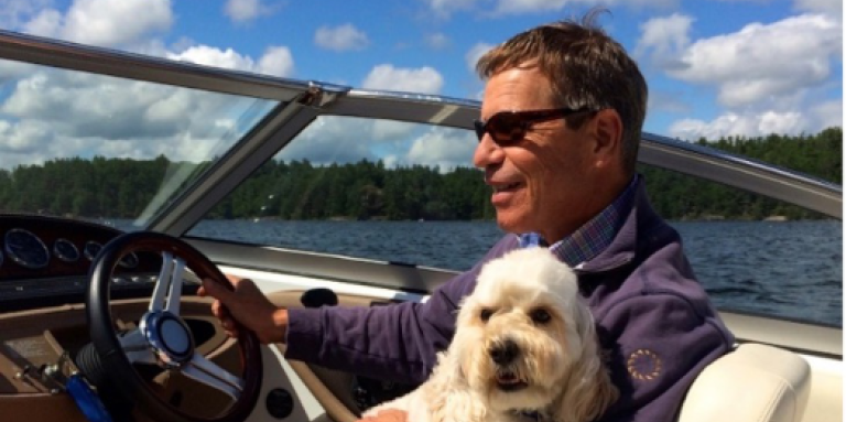Randall Oliphant is driving a boat with a dog on his lap.