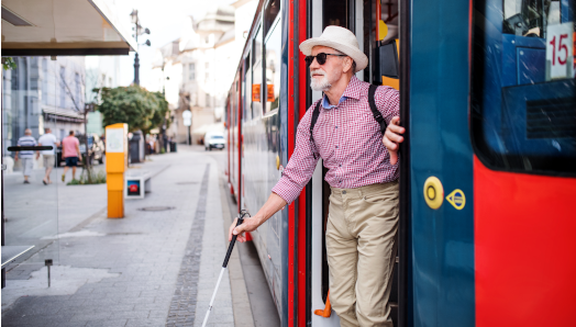 An older man using a white cane exits a city bus.