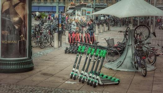 A city sidewalk with a row of electric scooters lined up on it.