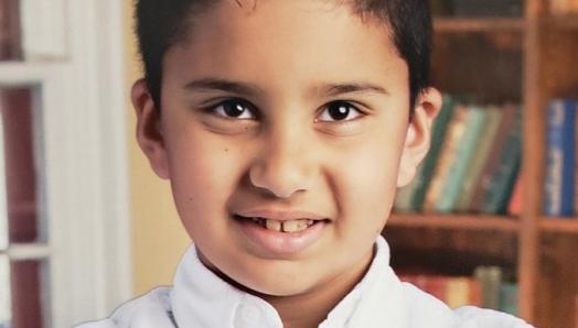 Ali Zaben, 9, poses for a school picture. He's smiling and crossing his arms. 