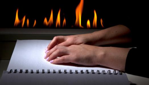 Hands move over a braille book. A fireplace emits flames in the background.