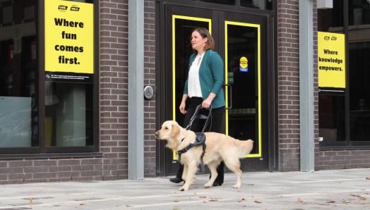 Erin Malone and her golden retriever guide dog, Winston, walking in front of a CNIB.