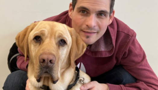 Ryan Hooey is crouched behind his Golden Labrador guide dog, Joe.