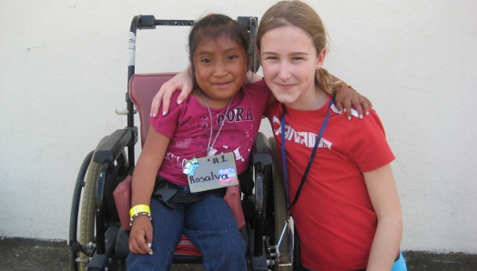 In Guatemala, a young Veronika crouches down next to a girl in a wheelchair. They have their arms around one another and pose for the photo.
