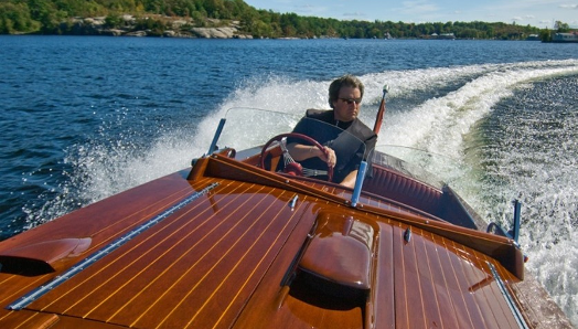 A man driving a wooden boat on a lake in Muskoka.