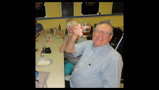 Wayne Laffin, sitting at a table with fellow guests at Legion Night at the Legion in MacTier, raising his glass with a big smile.