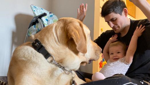 Ryan and his daughter Abigail, sitting on the floor playing with Joe, a CNIB Guide Dog.