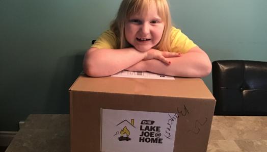 A young girl poses for a photo leaning on top of her camp-in-a-box, a cardboard box.