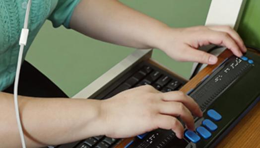 A woman using a braille keyboard while working at her computer.