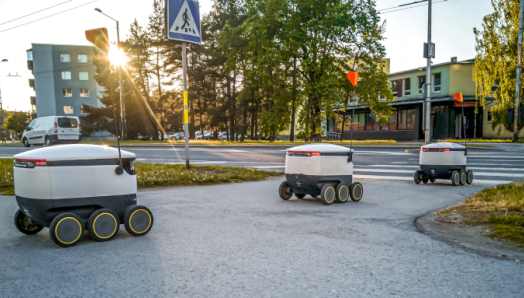 Three self-driving delivery robots drive along a city sidewalk.