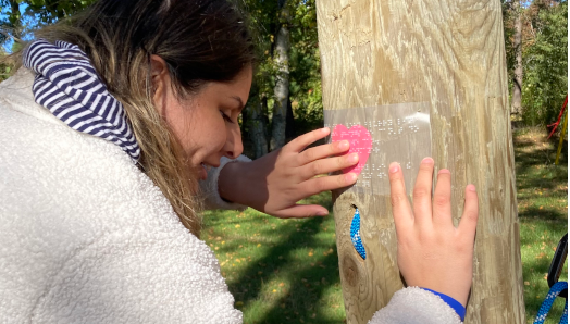A scavenger hunt clue is posted on the climbing wall at CNIB Lake Joe. The clue is written in braille and a young participant reads the braille clue with their hands.