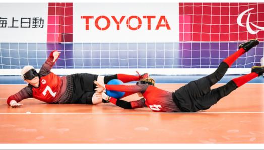 Team Canada goalball athletes Amy Burk, left, and Meghan Mahon, right, dive towards a ball in front of a net during the Tokyo 2021 Paralympic Games. Image courtesy of the Canadian Paralympic Committee.